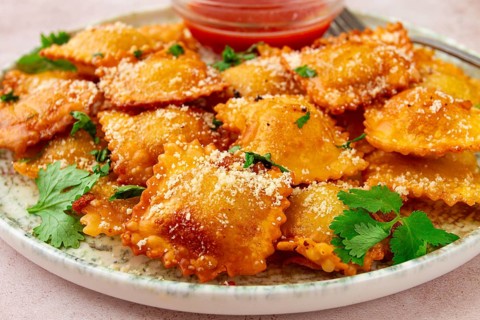 Fried ravioli with parmesan cheese, served with red sauce and garnished with herbs, on a light