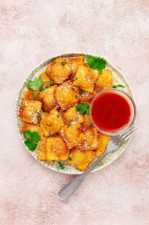 Fried ravioli with parmesan cheese, served with red sauce and garnished with herbs, on a light
