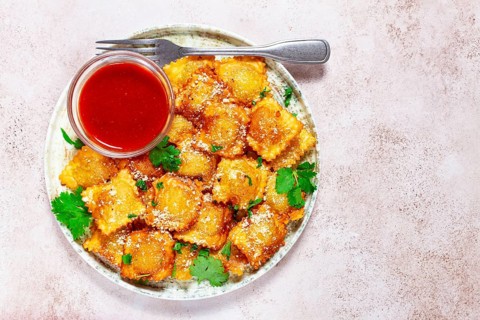 Fried ravioli with parmesan cheese, served with red sauce and garnished with herbs, on a light
