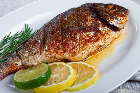 Baked dorado fish, in the oven, fried dorado, with spices and herbs, on a white plate, top view,