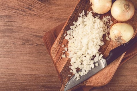 Finely chopped onion on a chopping board with a knife, wooden table, top view, no people