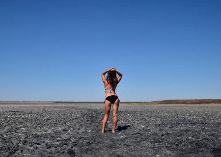Walk the dark-haired woman in a swimsuit on the bottom of a dry lake with salt and mud. Taman,