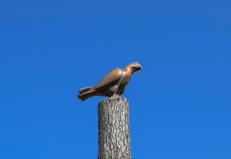 Figurine of a falcon on a stump of a tree against the blue sky. Taman, Krasnodar Krai, Russia