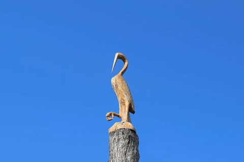 Figure of crane on the stump of a tree against the blue sky. Taman, Krasnodar Krai, Russia
