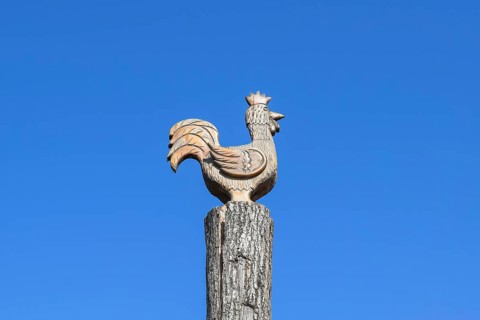 Figurine of a rooster on a tree stump on a background of blue sky. Taman, Krasnodar Krai, Russia