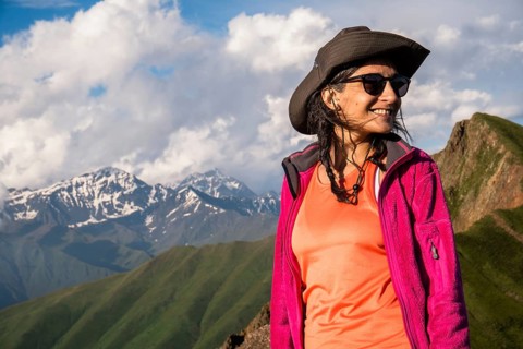 Happy Young Traveler hiker woman portrait wearing hat and jacket smiling in Kazbegi National Park