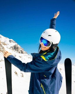 Young happy caucasian woman pose with skis arms outstretched in alpine zone. Get away skiing