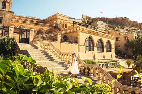 Traveler woman in white dress walking stairs of historic building - visit Mardin museum in old city