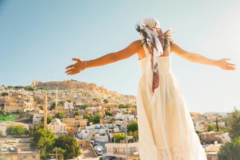 Traveler woman in white dress arms outstretched looking over panoramic view of historic city of