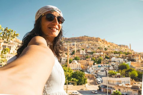Smiling woman in sunglasses taking selfie with panoramic skyline of historic Mardin Turkey and