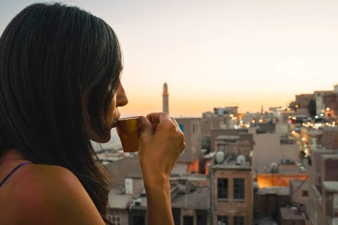 Tourist woman enjoying traditional Mirra coffee on rooftop with Mardin skyline and Mesopotamian