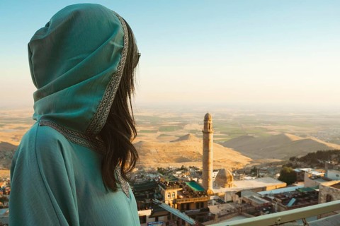Smiling woman traveler in abaya standing above Mardin Turkey with panoramic view of Mesopotamian