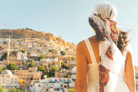 Traveler woman in white dress looking over panoramic view of historic city of Mardin Turkey with