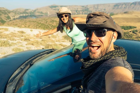 Happy young caucasian couple taking selfie while sitting in rented vehicle black car having road