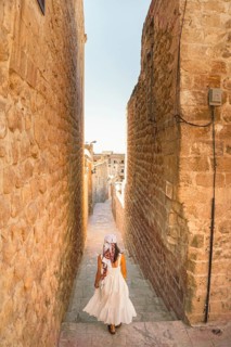 Traveler woman in white dress walking through narrow stone alley in historic city of Mardin Turkey