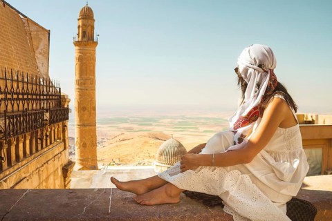 Traveler woman in white dress sitting near Great Mosque of Mardin Ulu Camii with panoramic view of