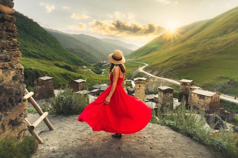 Woman in red dress looking at medieval towers of Ushguli Georgia during sunset with mountains and