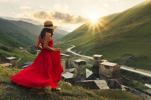 Woman in red dress looking at medieval towers of Ushguli Georgia during sunset with mountains and