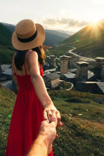 Young Couple holding hands leading way in Ushguli Georgia woman in red dress leading towards