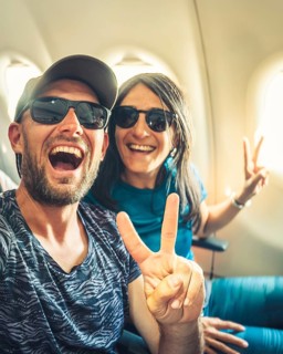 Happy casual dressed tourist taking selfie inside airplane - Cheerful couple on summer vacation -