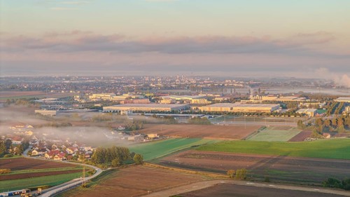 An extensive industrial area becomes visible in the morning sun. Fog envelops the landscape and the