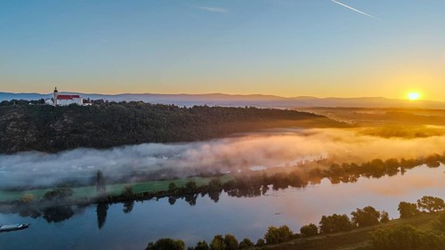 The sunrise bathes the Danube in warm light. A light mist hovers over the water, while the