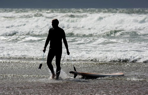 Silhouette Of A Surfer With His Surfboard Leaving Water Of Cold Atlantic At The Coast Of Ireland