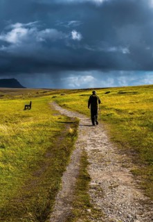 Old Man With Walking Stick Strolls On Narrow Gravel Path Through Scenic Landscape With Spectacular