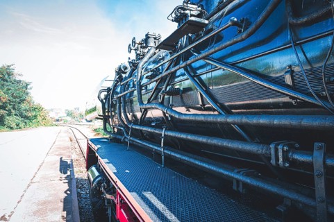 Partial view of a shiny steam locomotive showing the detailed mechanics and the railway landscape,