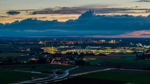 The scene shows an expansive landscape at dusk. Illuminated buildings and streets are visible in