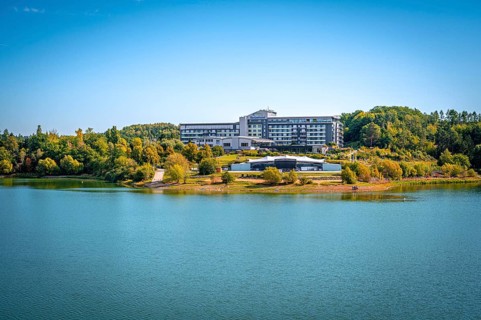 Organic lakeside hotel surrounded by trees under a clear blue sky, Zeulenrodaer Meer reservoir,