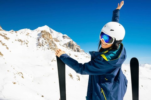 Young happy caucasian woman pose with skis looking at camera hands up in alpine zone. Get away