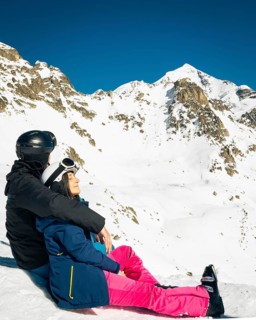 Young caucasian couple pose sits hug enjoying looking at snowy mountains in winter. Get away skiing