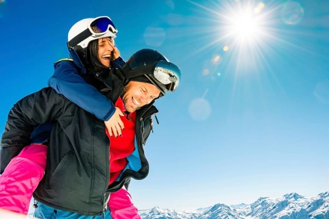 Happy young caucasian skiers couple in love having fun together playing in mountains piggybacking