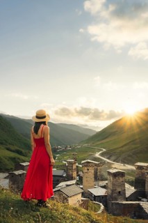 Young pretty Woman traveler in red dress looking at medieval towers of Ushguli Georgia during