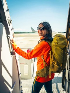 Young happy caucasian female traveler backpacker with carry on hiking backpack boarding airplane