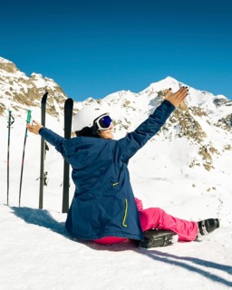 Young happy caucasian woman pose with skis arms outstretched in alpine zone. Get away skiing