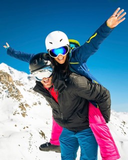 Happy young caucasian skiers couple in love having fun together playing in mountains piggybacking