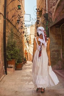 Traveler woman in white dress walking through narrow stone alley in historic city of Mardin Turkey