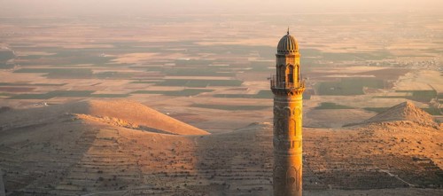 Historic Ulu Cami mosque minaret in Mardin Turkey illuminated by sunset against vast Mesopotamian
