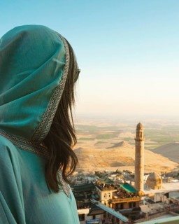 Smiling woman traveler in abaya standing above Mardin Turkey with panoramic view of Mesopotamian