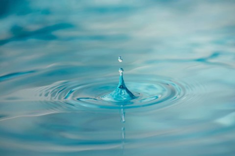 Water Drop Creates Circular Waves on Calm Surface Of Blue Water