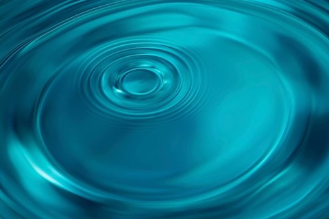 Water Drop Creates Circular Waves on Calm Surface Of Blue Water