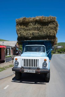 A blue lorry loaded with several layers of hay bales is parked on a country road, Armenia