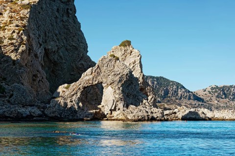 Stone arch at Grande blue beach with clear blue water and sunny sky, showing a natural and peaceful