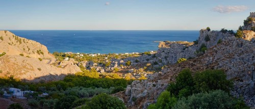 Coastal landscape of Stgna overlooking the sea, framed by rocky hills and lush vegetation, under a