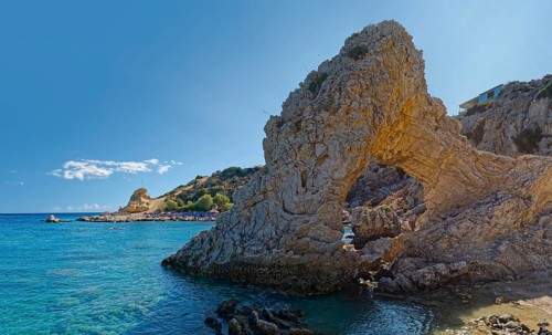 Grande Blue coast with a natural stone arch in front of clear blue water under a sunny sky, Grande