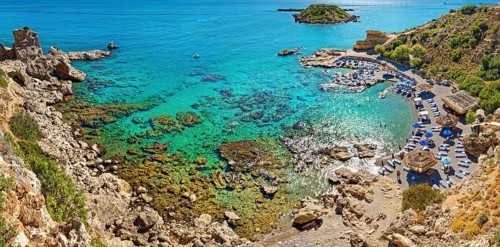 Secluded Grande Blue Bay with clear turquoise water and rocks, along which a row of beach loungers