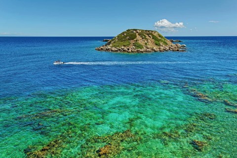 Small island Vrachonisida in front of the Grande Blue Beach in the turquoise blue sea with passing