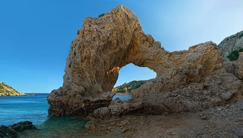Rock arch at Grande Blue Beach under a clear blue sky in a sunny coastal landscape, Grande Blue